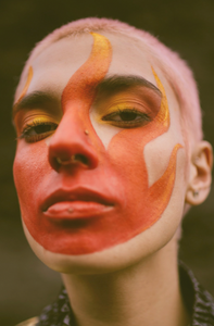 Close-up picture of an androgynous person wearing Nöz Sunfire Orange and Sunny Daze Yellow sunscreen to look like flames.