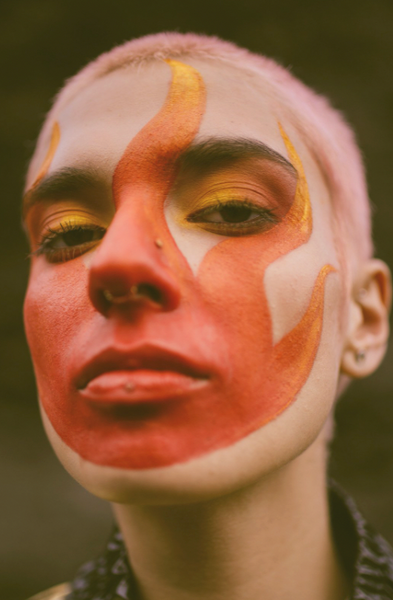 Close-up picture of an androgynous person wearing Nöz Sunfire Orange and Sunny Daze Yellow sunscreen to look like flames.